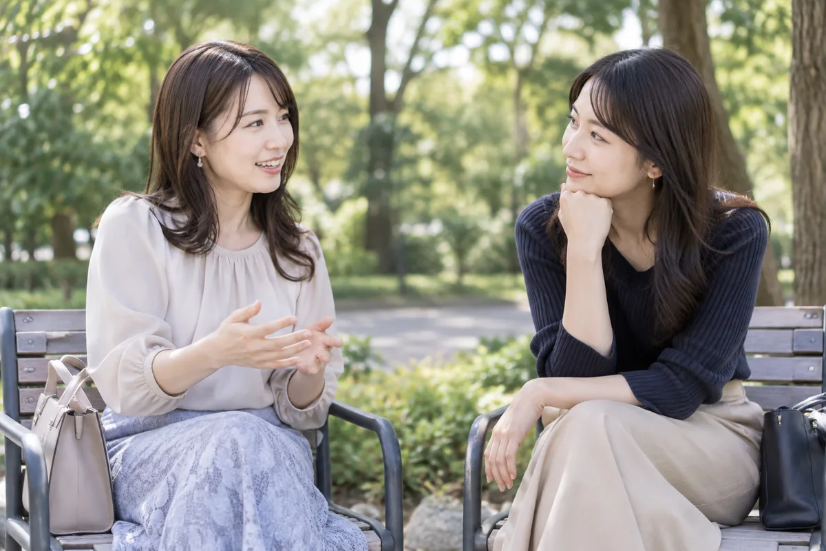 公園の椅子で個人的な知らせを静かに伝え合う二人の女性