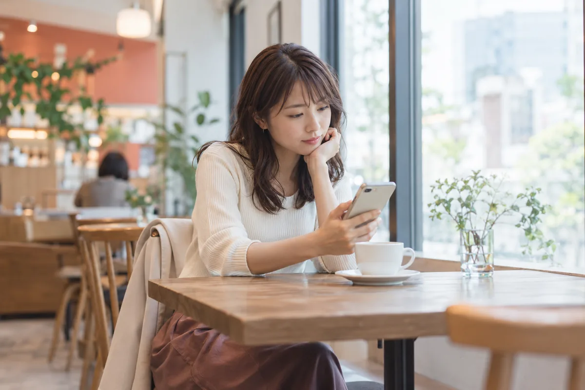 カフェでスマートフォンを見ながら待ち合わせを考える女性