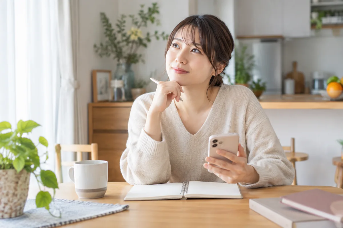 相談方法を考えながらスマートフォンとノートを手にする女性